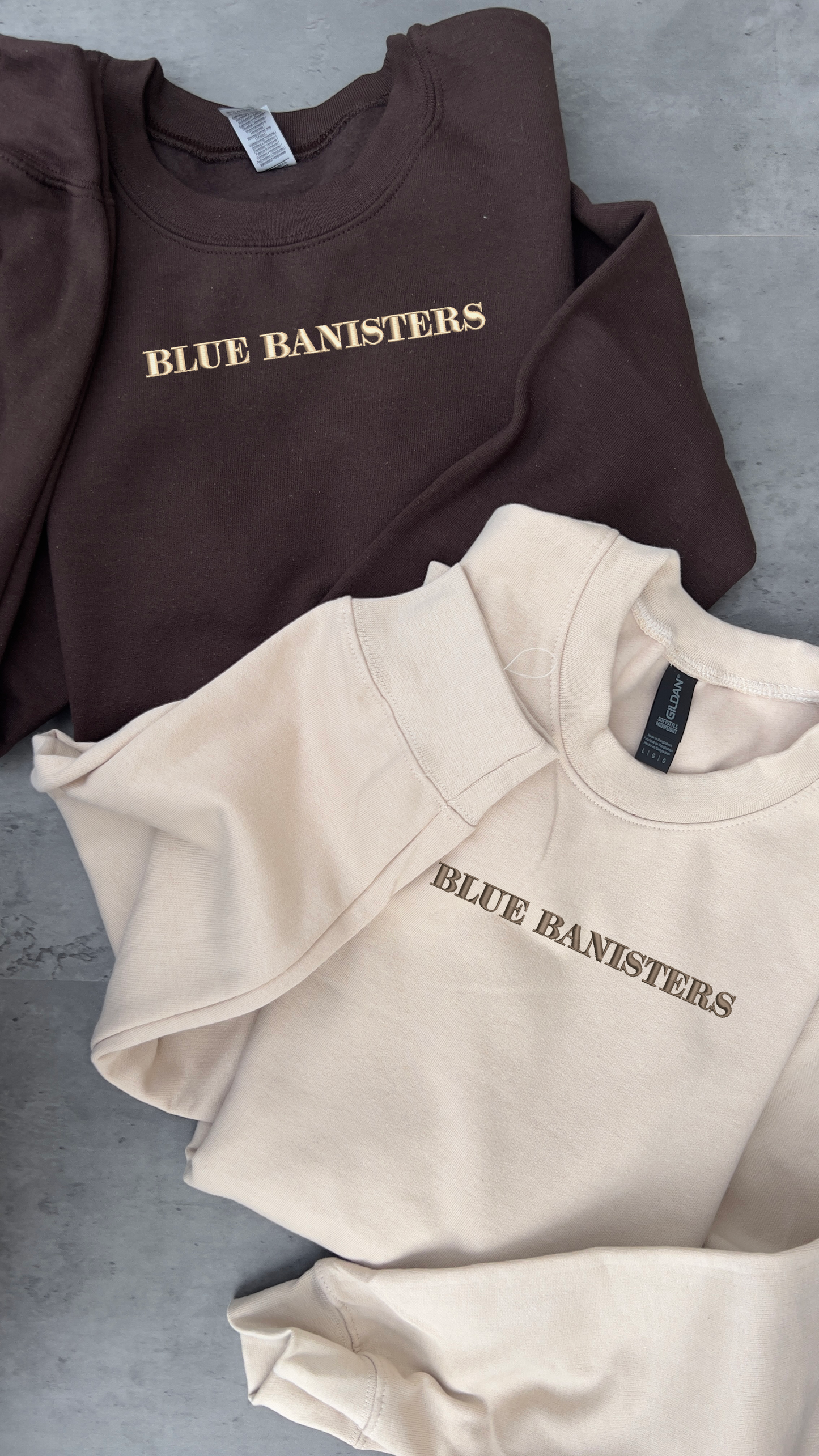 dark brown sweatshirt with a cream embroidery of blue bannisters and a cream coloured sweatshirt with a dark blank del rey sweatshirts, brown embroidery of blue bannisters 