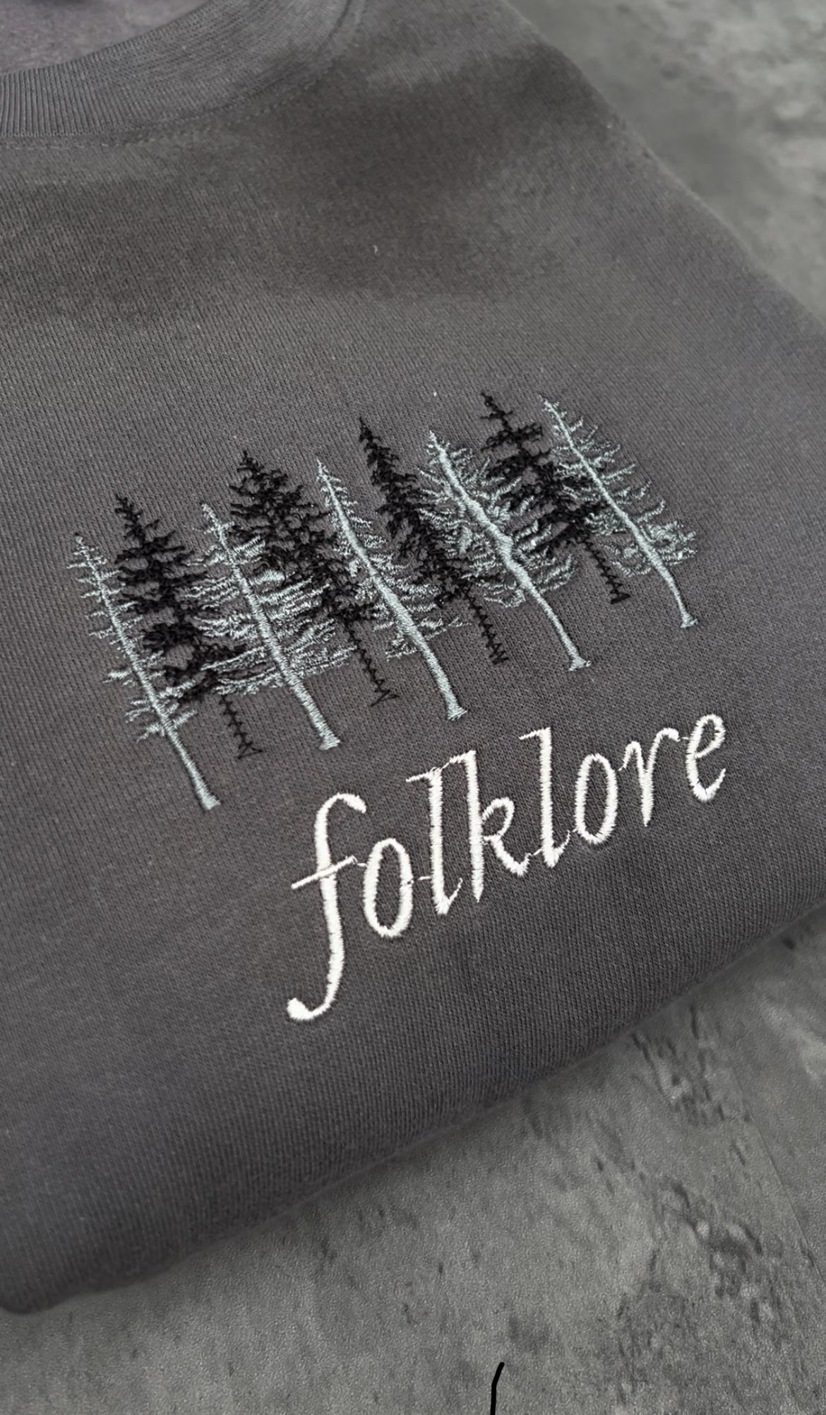 folklore album embroidery by taylorswift with tree in the background of the title on a dark grey sweatshirt