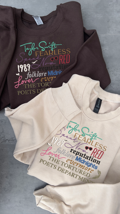 Taylor Swifts albums all embroidered onto a sweatshit using their individual colours and fonts specific to their album covers 