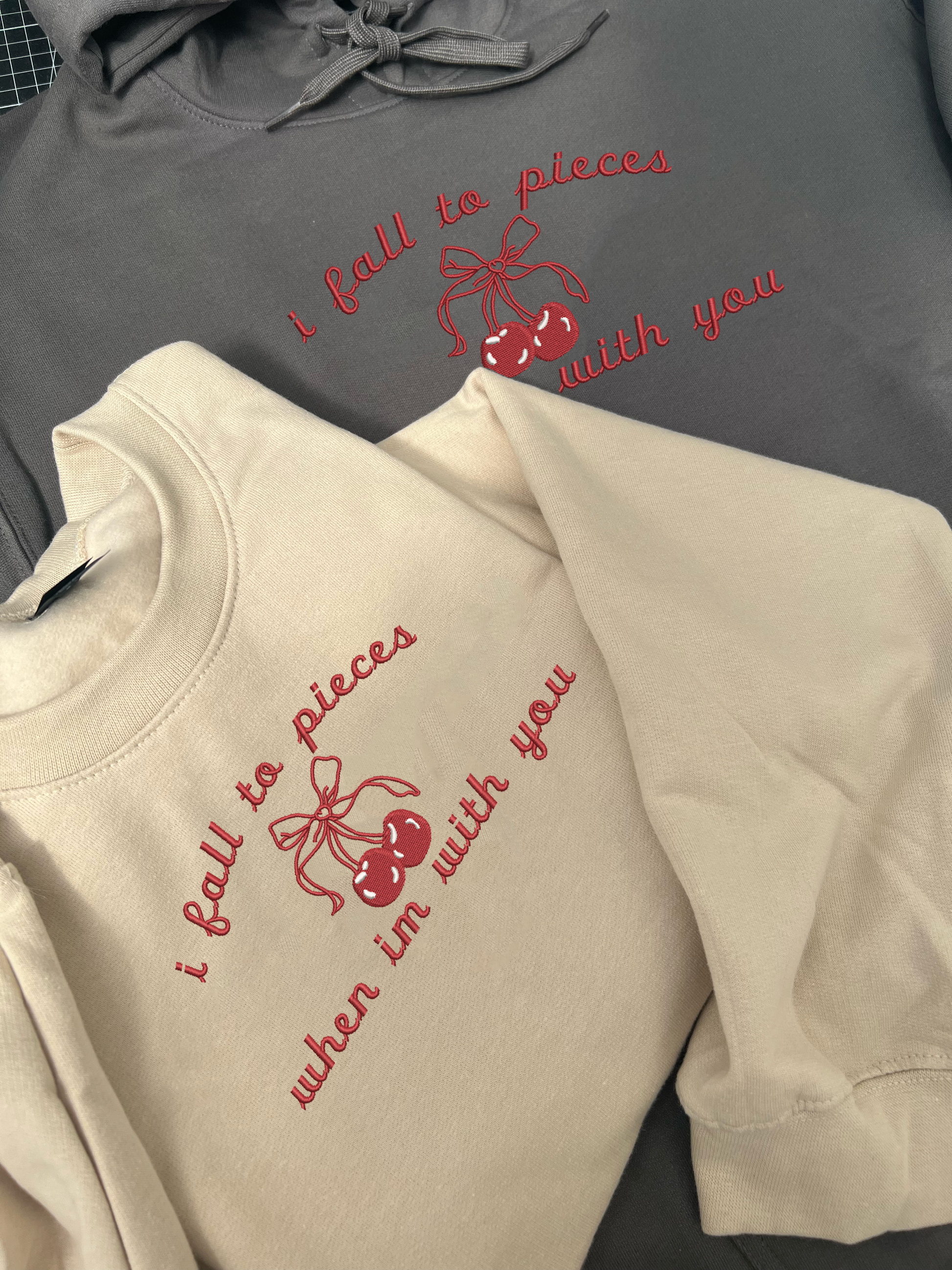 lana del rey lyric ' I fall to pieces when im with you ' with a cherry with a bow all embroidered in red thread on the centre chest of a sweatshirt in a beige colour 