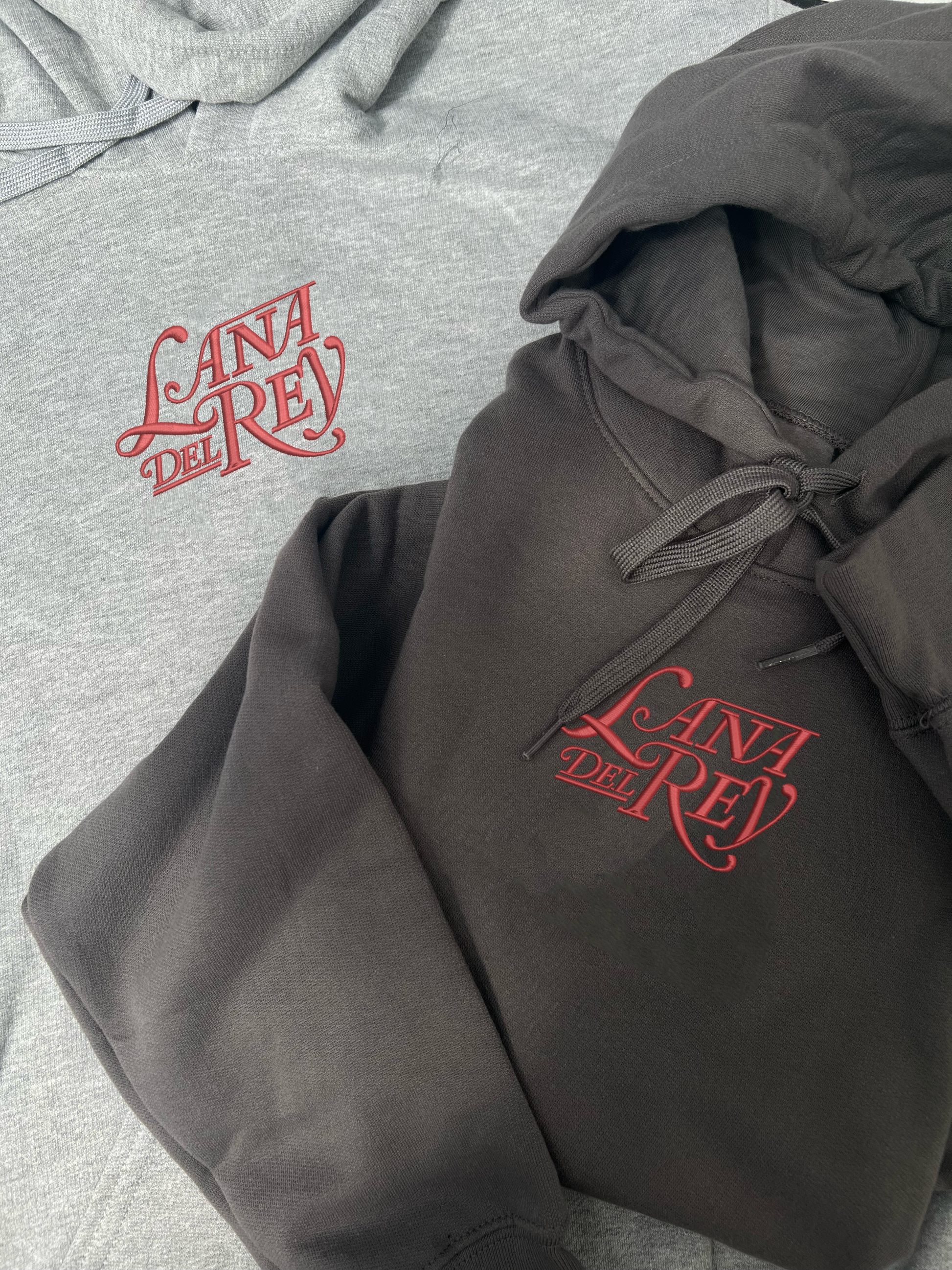 lana del rey embroidered in the lust for life font on the centre of the chest in red thread on a dark grey and light grey hoodie 