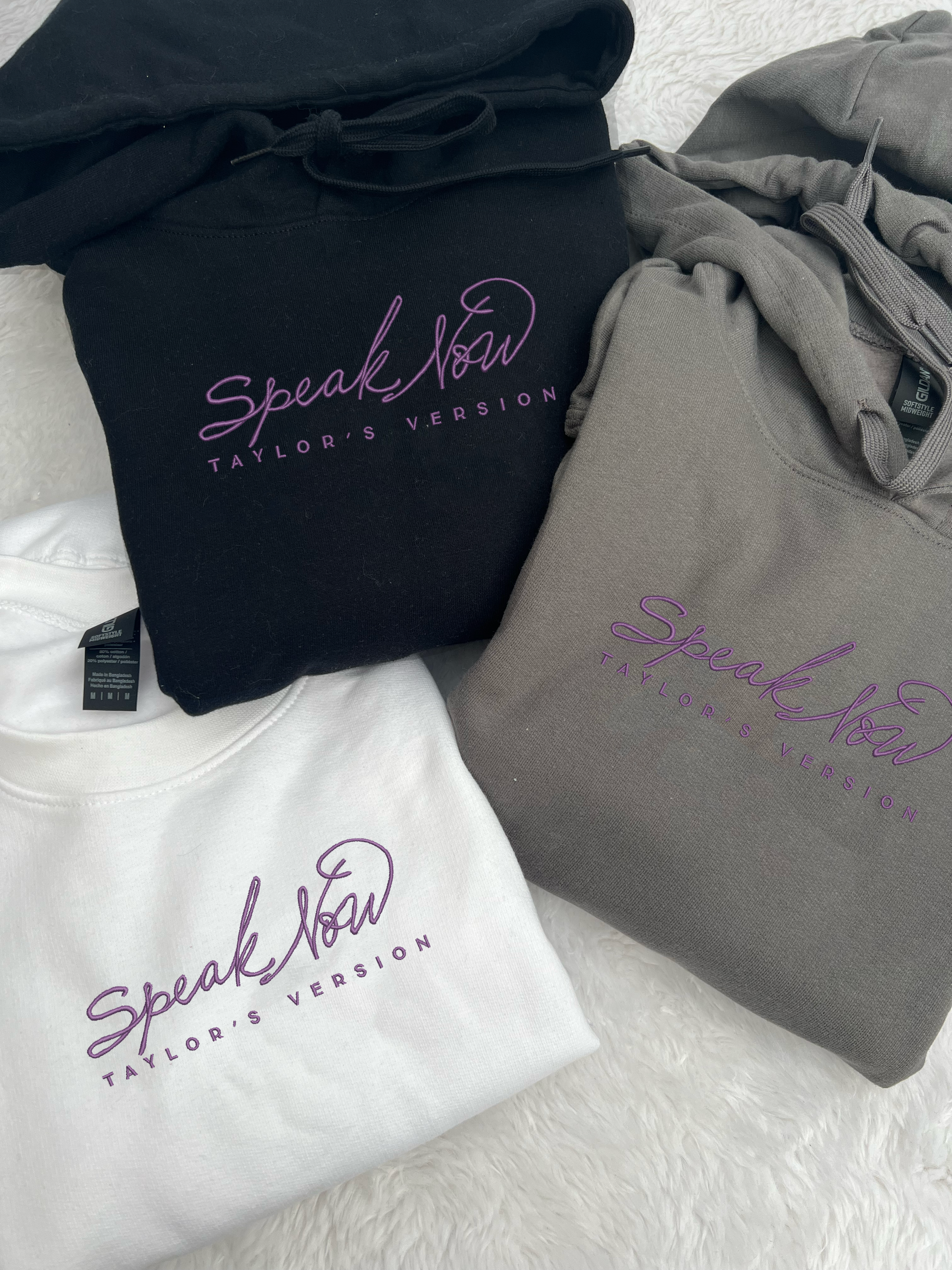 taylor swifts speak now album title embroidered in the same font and colour as appears on album cover on a black , white and dark grey coloured hoodie